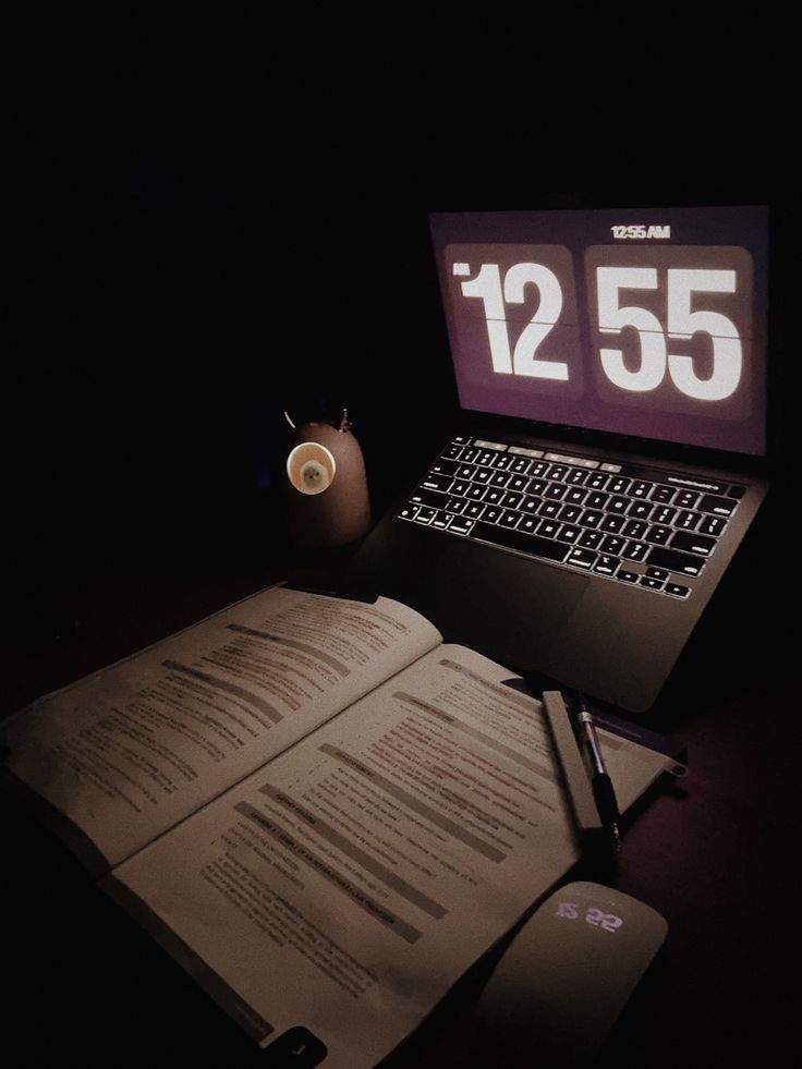 an open laptop computer sitting on top of a desk next to a book and pen