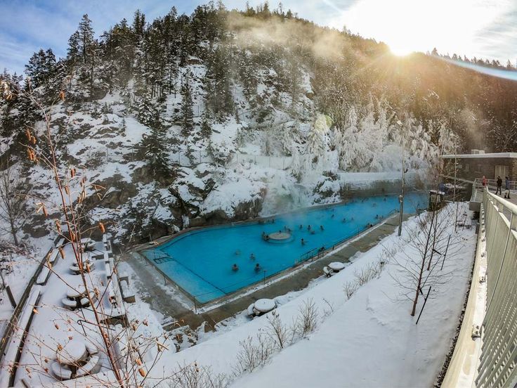 an aerial view of a swimming pool surrounded by snow covered trees and mountains in the background