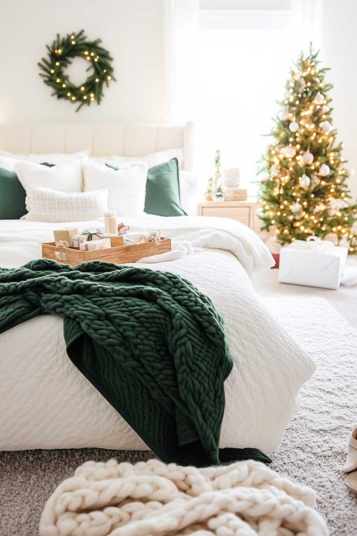 a christmas tree is in the corner of a bedroom with white bedding and green blankets