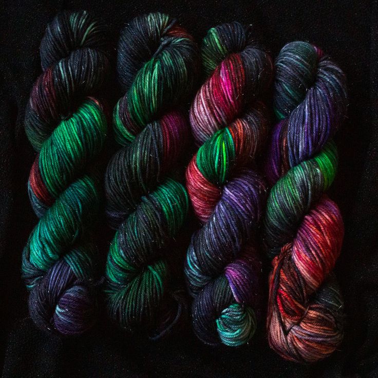 several skeins of yarn in different colors on a black surface with one green and the other red