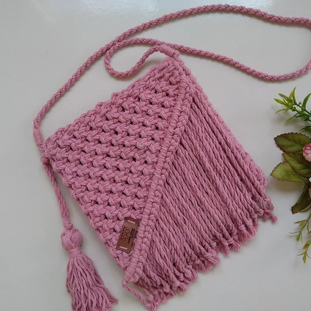 a pink crocheted purse sitting on top of a white table next to flowers