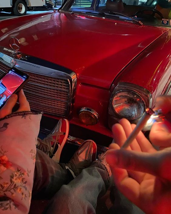 a person sitting in front of a red car holding a cell phone and writing on it