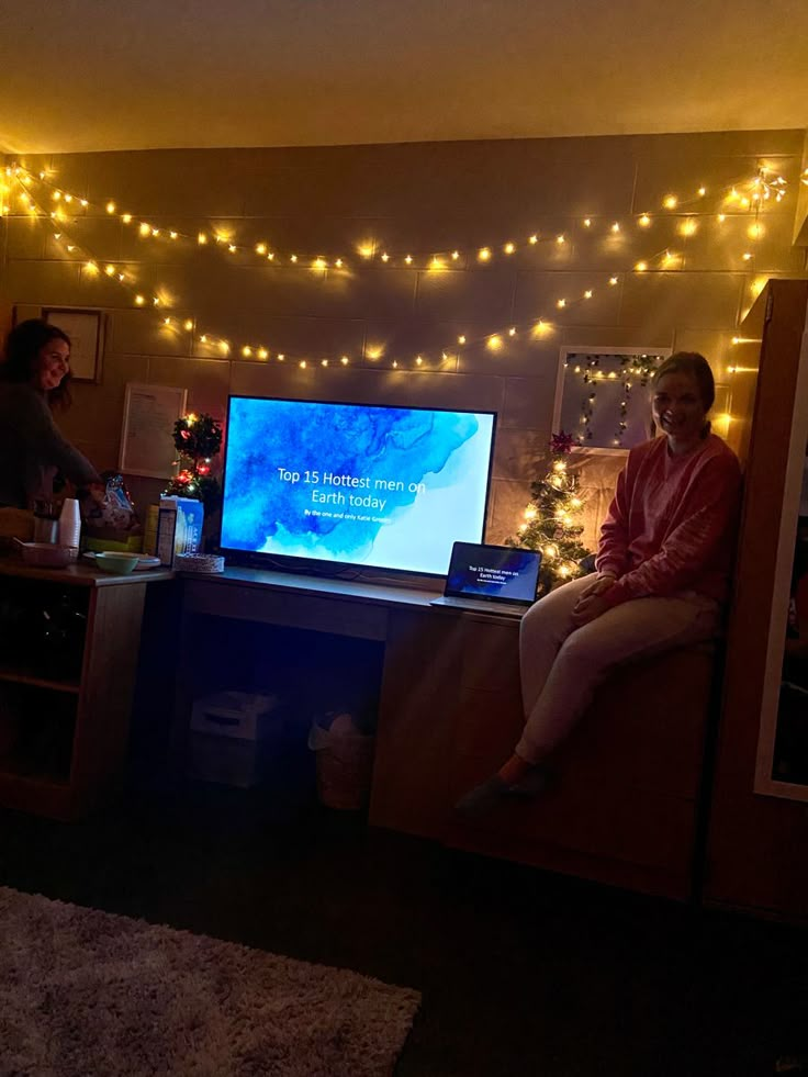 two women sitting in front of a flat screen tv with christmas lights on the wall