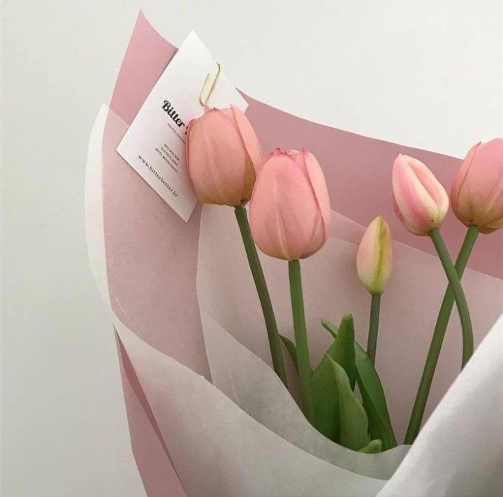 pink tulips are wrapped in white paper with a tag on it, and the flowers are still blooming