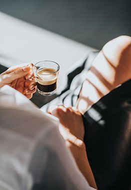 a person holding a cup of coffee in their hand while sitting on a couch with the sun shining down