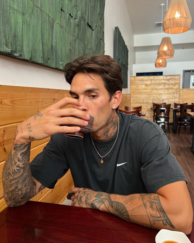 a man sitting at a wooden table drinking from a glass in front of his face