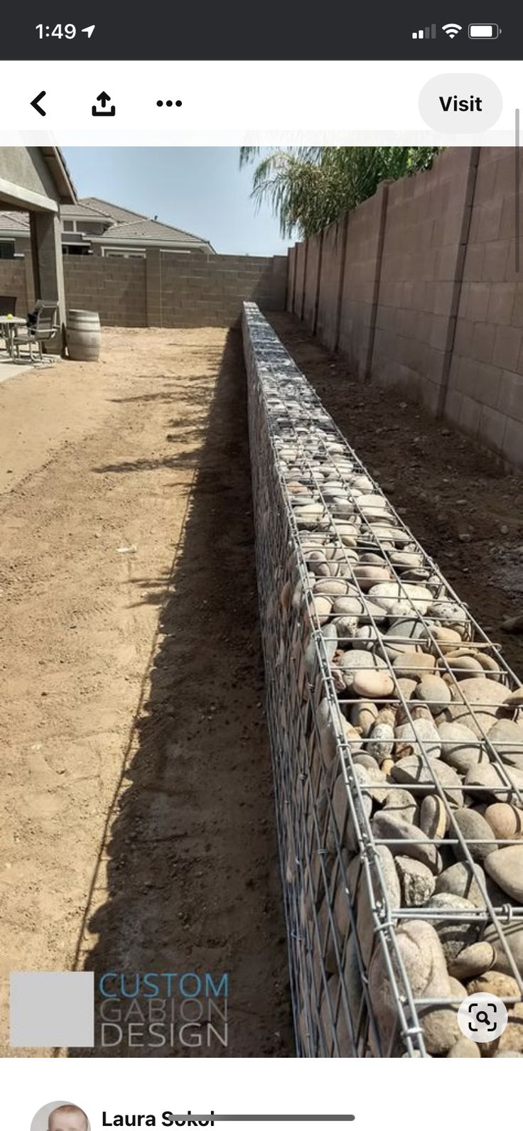 a fence made out of rocks sitting on the side of a dirt road next to a building