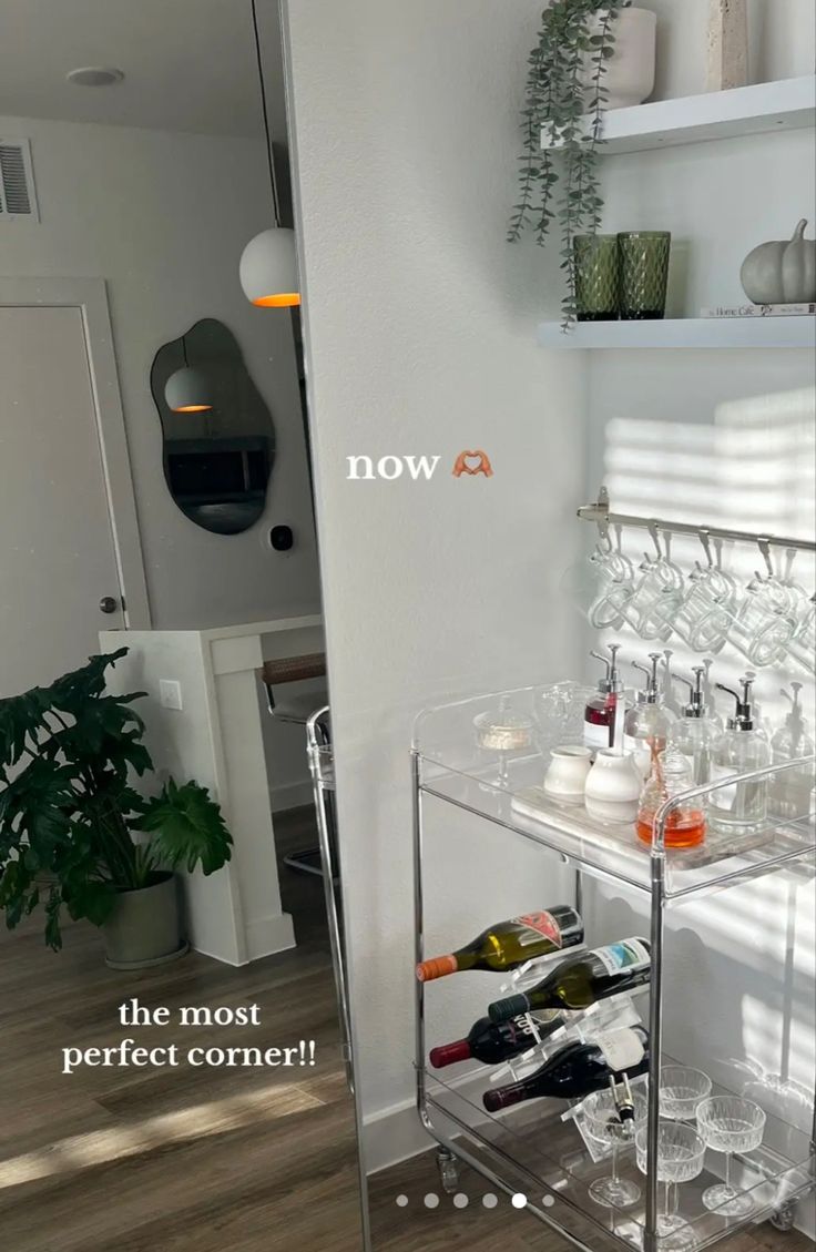 a bar cart filled with bottles and glasses on top of a wooden floor next to a white wall