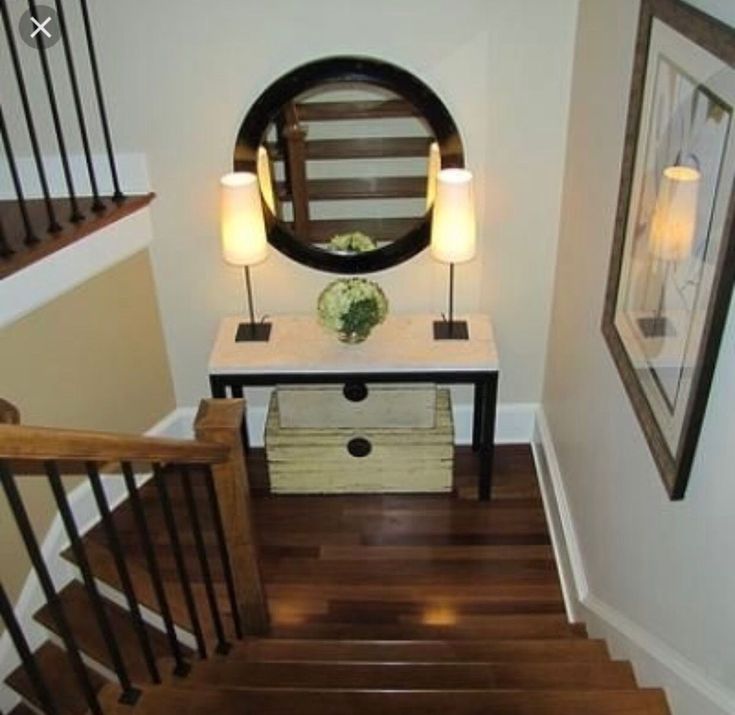 there is a mirror on the wall next to some stairs and a table with drawers