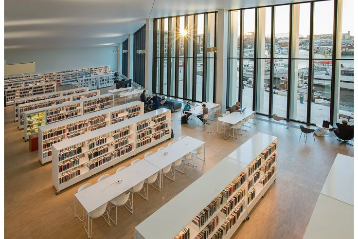 a library filled with lots of white tables next to tall windows and bookshelves