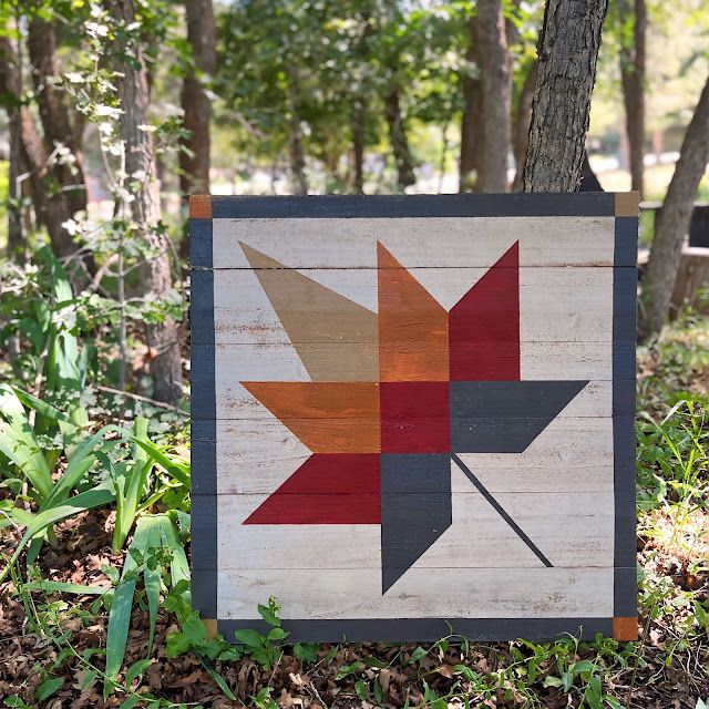 a wooden sign with a maple leaf on it in the grass next to some trees