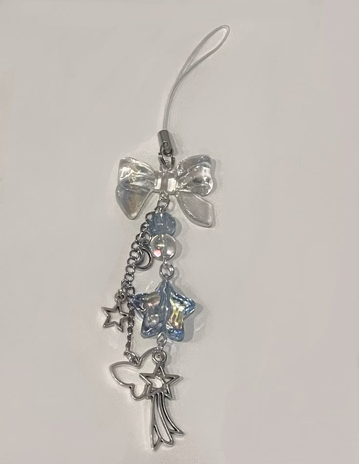 a pair of earrings with charms attached to them on a white surface, one has a bow and the other has an angel