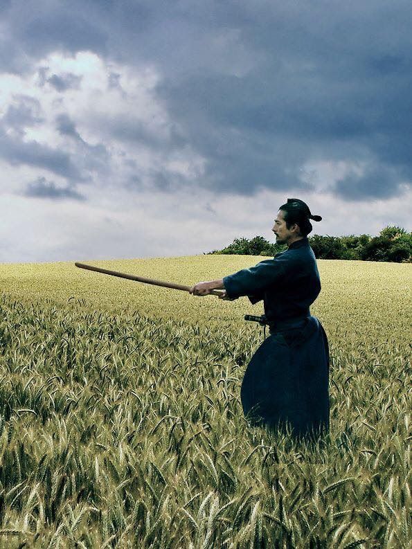 a person in a field holding a stick with one hand and looking up at the sky