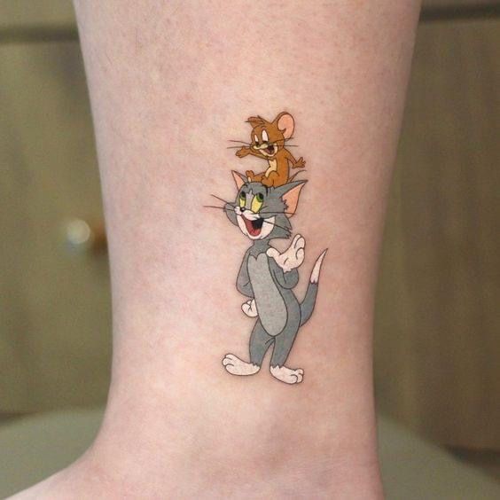 a cartoon tattoo on the ankle of a woman's leg shows an image of a cat and mouse