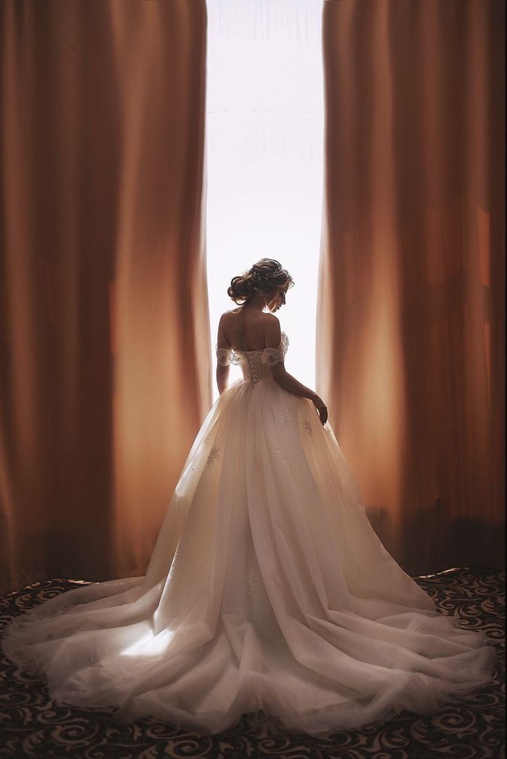 a woman in a wedding dress is standing by the window with her back to the camera