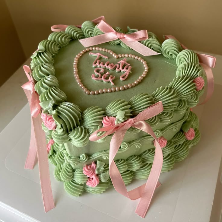 a heart shaped cake decorated with green icing and pink ribbon on top of a white table