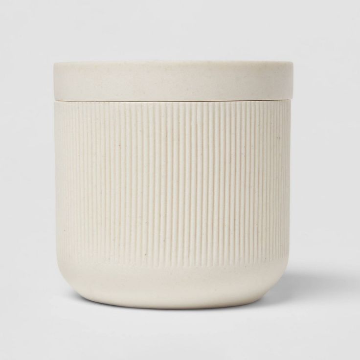 a white ceramic container with ribbed design on the front and bottom, sitting on a white surface