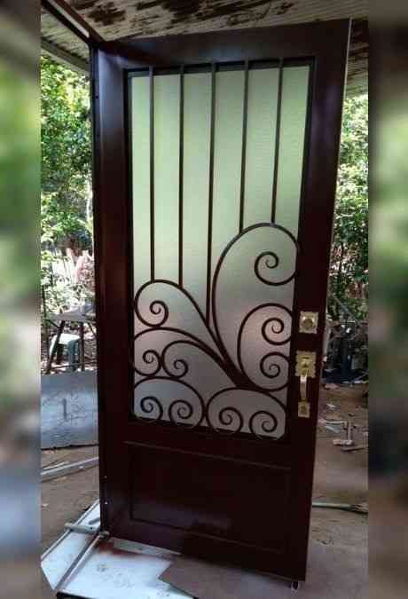 a brown door with white swirls and glass on the top part, in front of a house