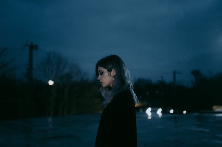 a woman standing in the middle of a street at night with her head turned to the side