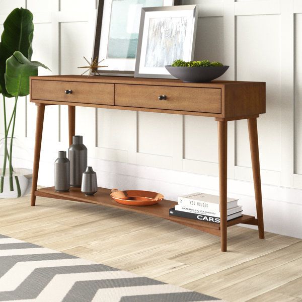 a wooden table with two drawers and a plant on it next to a white wall