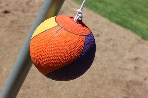 an orange and purple ball hanging from a metal pole on a playground area with grass in the background