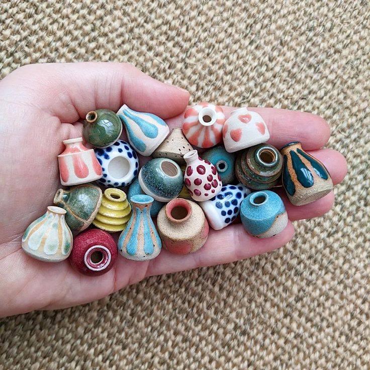 a hand is holding several small ceramic vases in it's palm, and there are many different colors on the beads