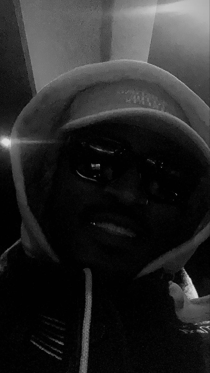 a black and white photo of a person wearing a hat, sunglasses and a hoodie