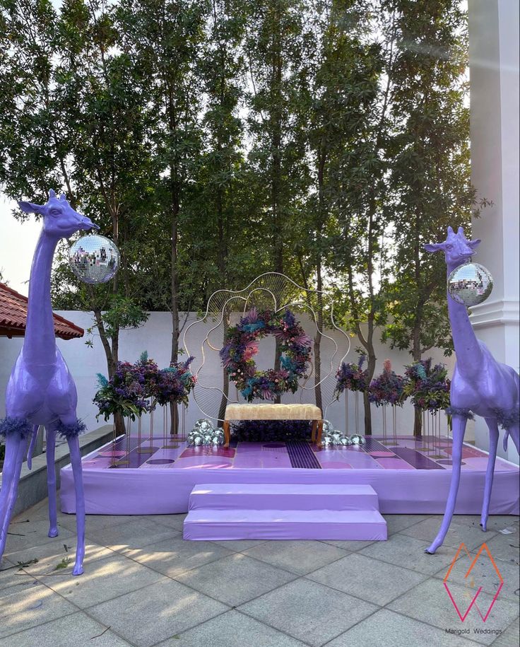 two purple giraffes are standing in front of a stage with flowers on it