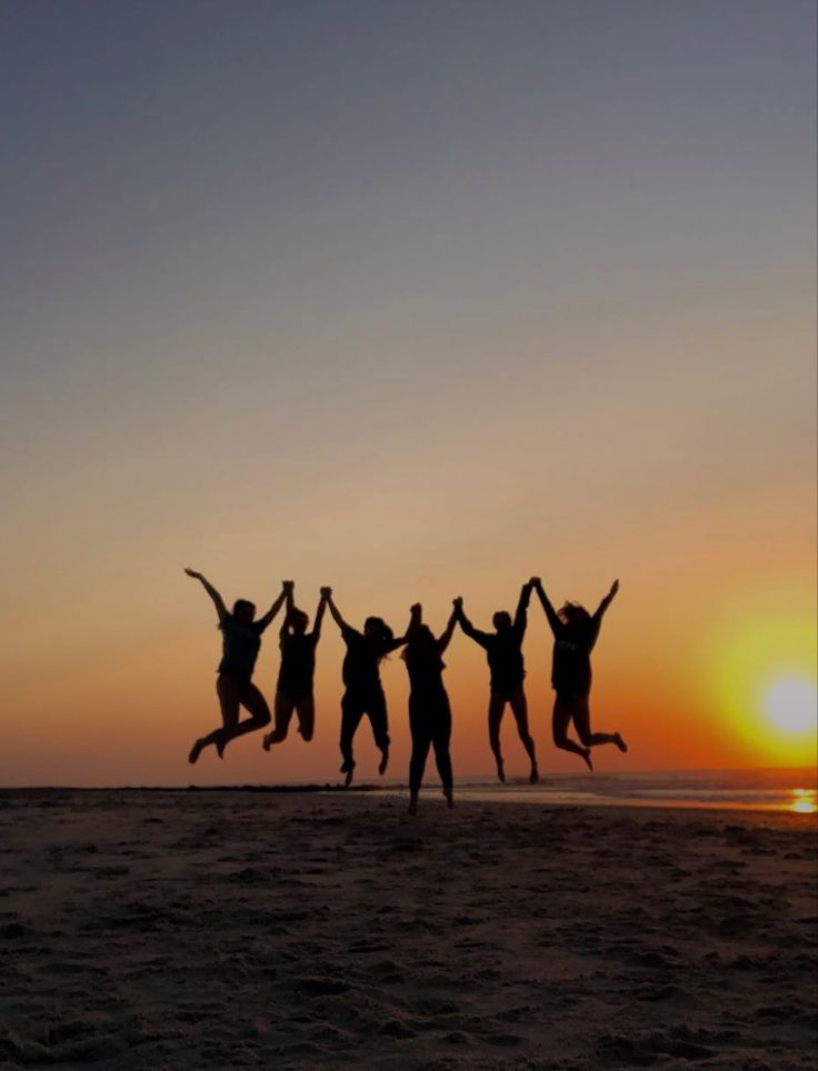 four people jumping in the air on a beach at sunset