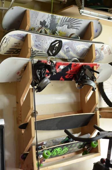 several snowboards and skis are stored in a storage rack on the wall above a bicycle