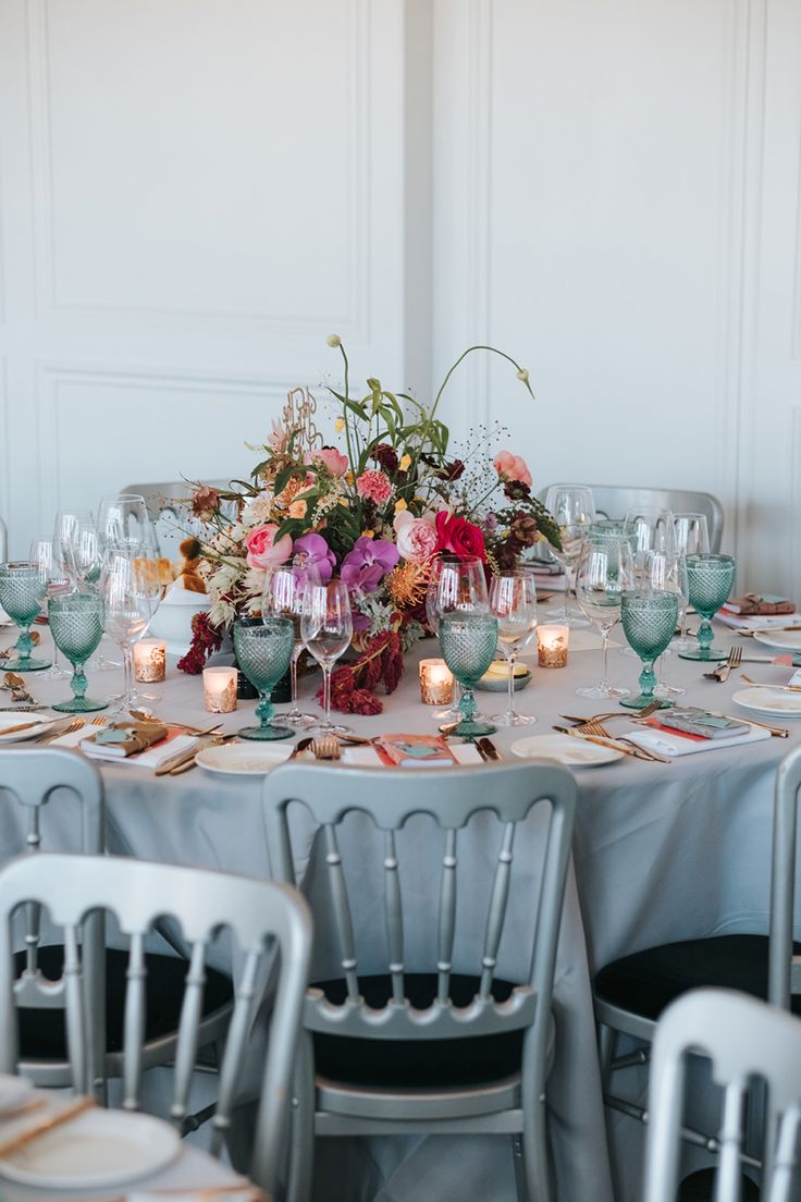 the table is set with silver chairs and flowers in vases, candles, and wine glasses