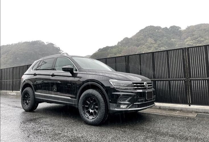 a black volkswagen suv parked in front of a fence on a rainy day with mountains in the background