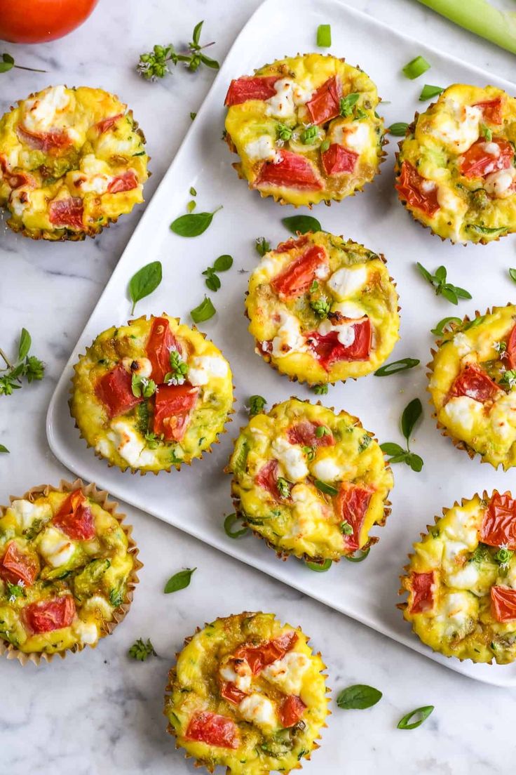 several muffins with tomatoes and cheese on a tray next to some fresh vegetables