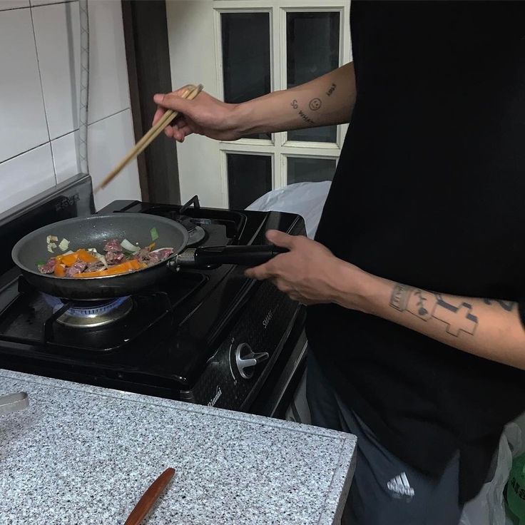 a man cooking food in a wok on top of a stove with chopsticks