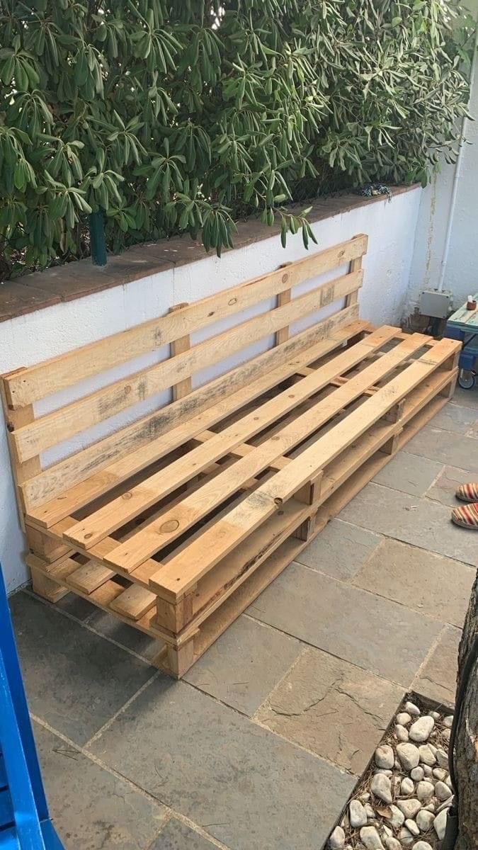 a wooden bench sitting on top of a stone floor next to a blue trash can