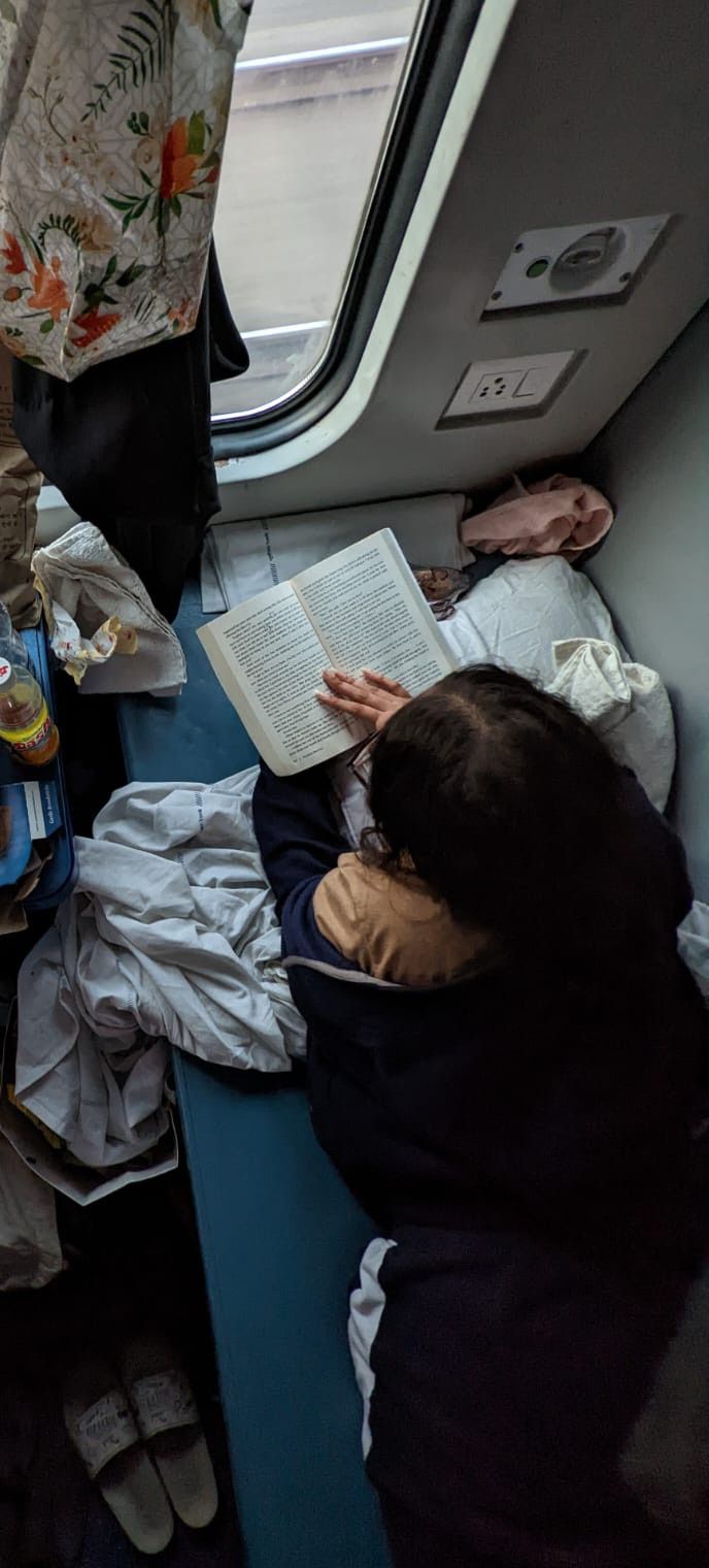 a woman reading a book while sitting on a train next to another person with an open book