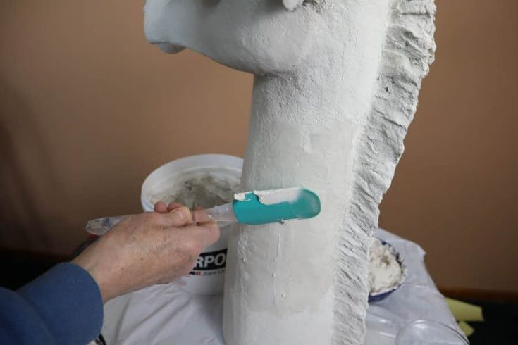 a person is painting a horse head on a white pillar with blue paintbrushes