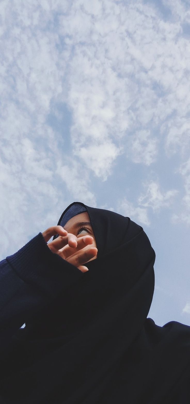 a person wearing a black hoodie is holding their hand up to the sky with clouds in the background