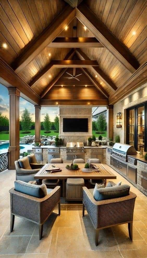 an outdoor kitchen and dining area with wood ceilinging, stone flooring and large windows