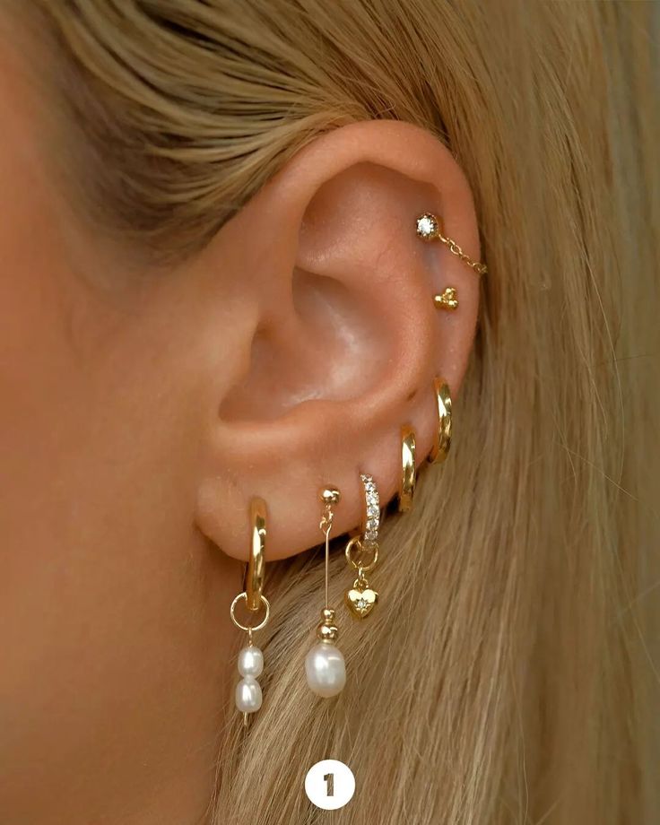 a close up of a person wearing ear piercings with pearls and gold chains on them