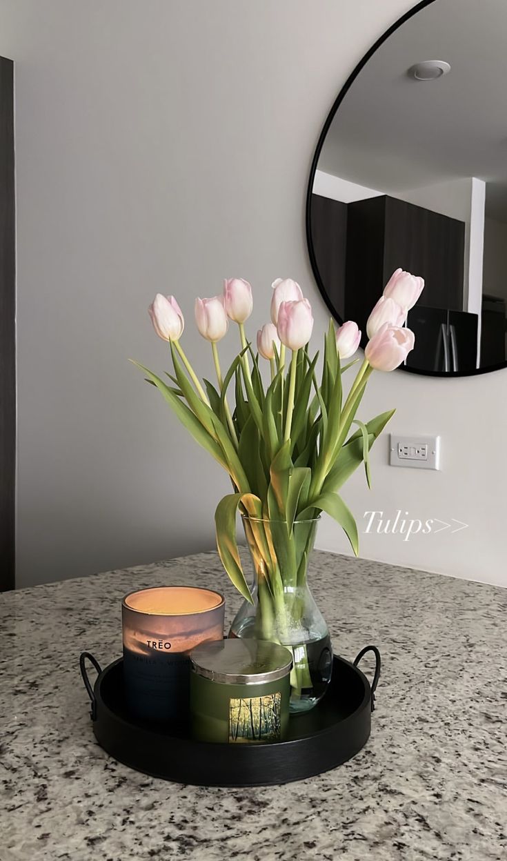 a vase filled with pink flowers sitting on top of a counter next to a mirror