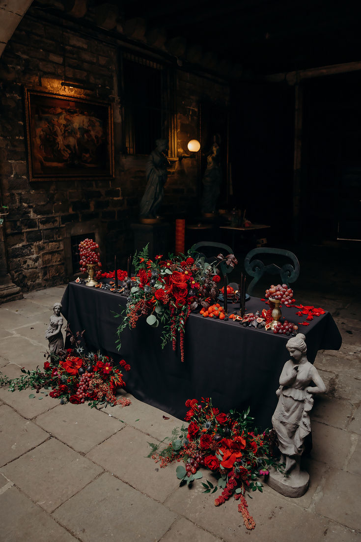 a table with red flowers and candles on it in front of a stone building at night