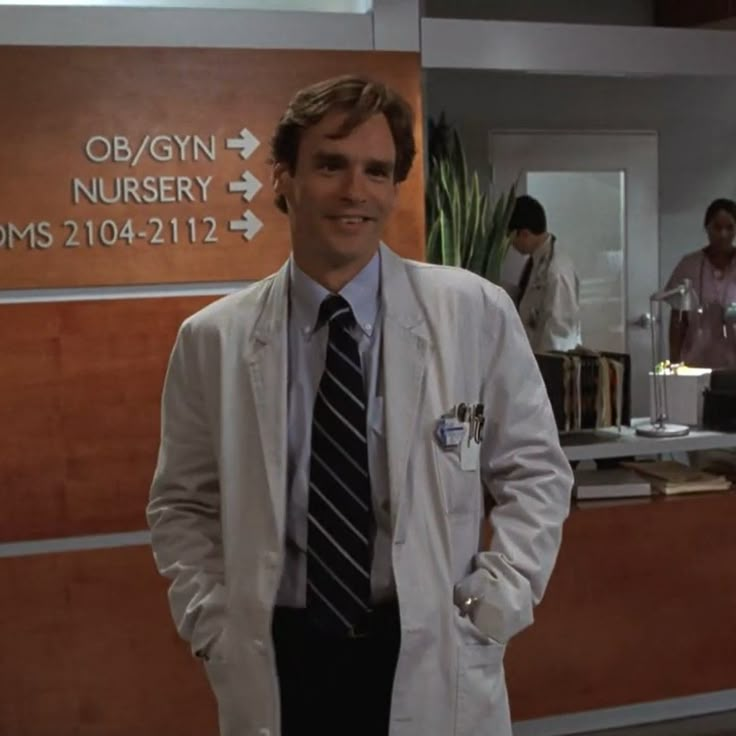 a man in a white lab coat and tie standing next to a wall with signs on it