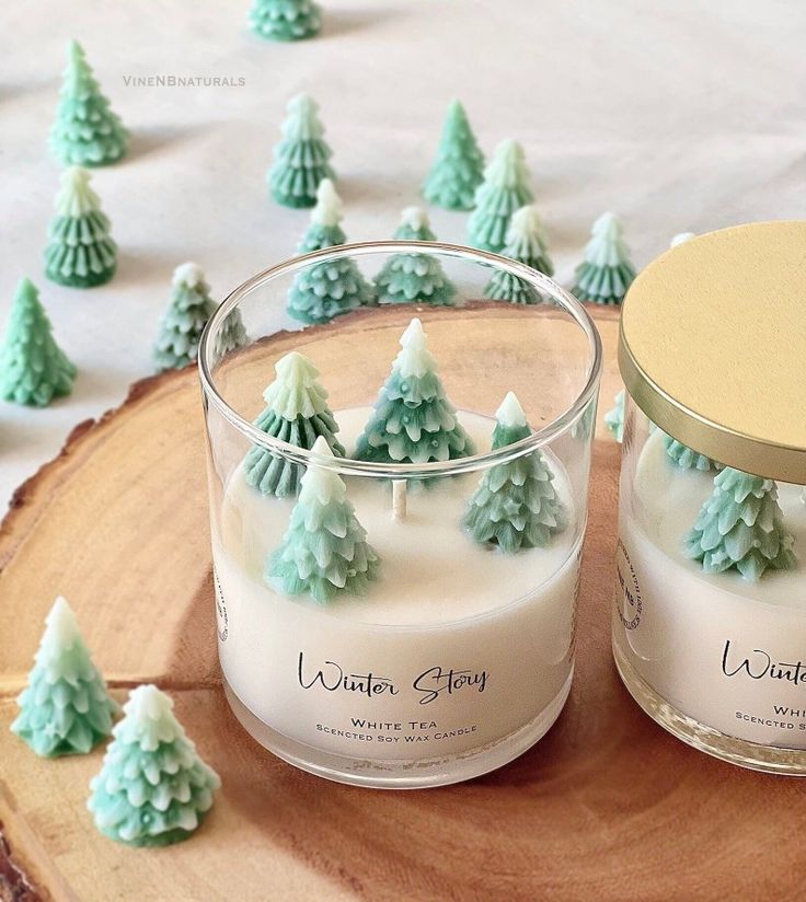 two candles sitting next to each other on top of a wooden table covered in frosted trees