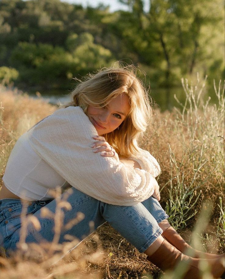 a woman is sitting in the grass with her legs crossed and looking at the camera