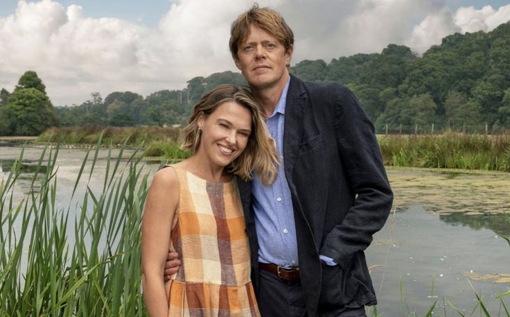 a man and woman standing next to each other in front of a pond with water lilies