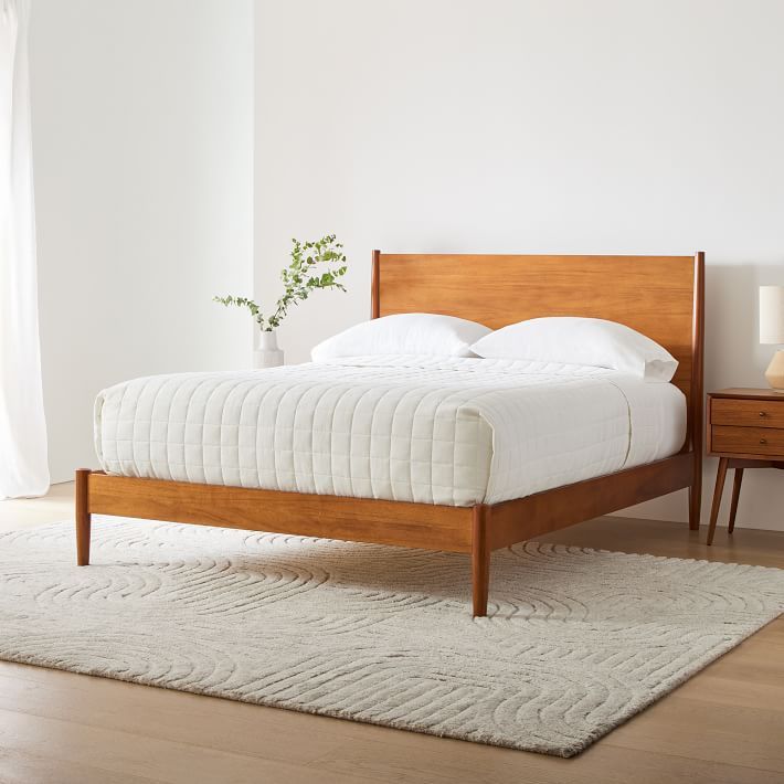 a bed sitting on top of a white rug next to a wooden dresser and lamp