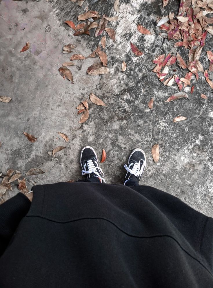 a person standing on top of a sidewalk next to leaves