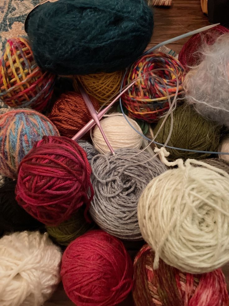 several skeins of yarn are on the floor next to balls of yarn and knitting needles