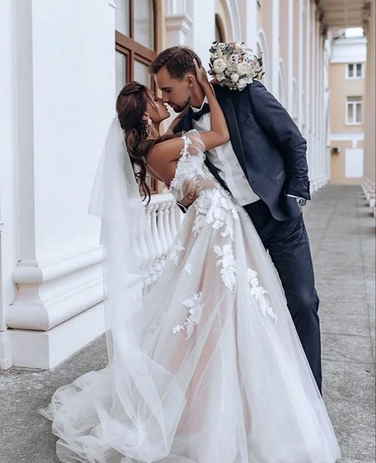 a bride and groom kissing in front of a white building with columns on either side